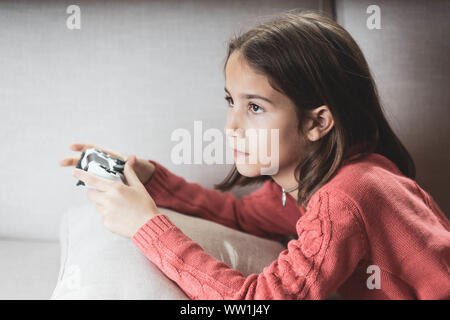 Niña jugando en casa con la videoconsola tumbada en el divani Foto Stock