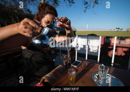 Una donna che serve tè tradizionalmente nella terrazza di un caffè di Marrakesh, Marocco. Foto Stock
