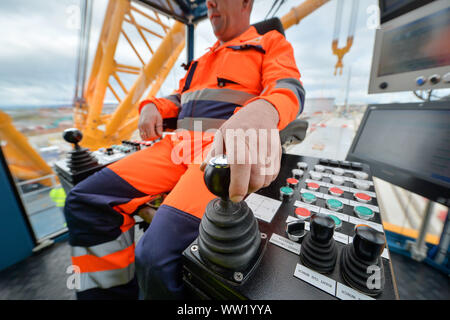 Il gruista Martin Redmond si alterna il joysick dentro la sua cabina a bordo di "Big Carl', il più grande del mondo di gru che si appresta ad iniziare i lavori a Hinkley Point C power station in Somerset. In grado di sopportare fino a 250m di altezza, il Sarens SCC-250 gru può raggiungere maggiore del più alto tower presso il London Canary Wharf e può trasportare 5.000 tonnellate in un ascensore singolo. Foto Stock