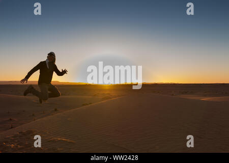 Un uomo retroilluminato salta felicemente in Erg Chebbi deserto all'alba Foto Stock