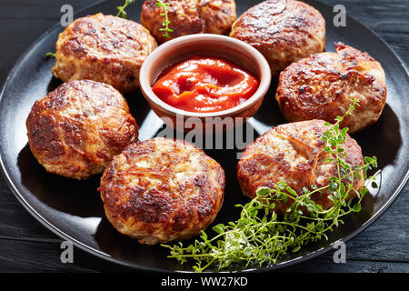 Stufato di cavolo con fette di salsicce fritte servite su una piastra su un tavoli in legno nero, vista da sopra, close-up Foto Stock