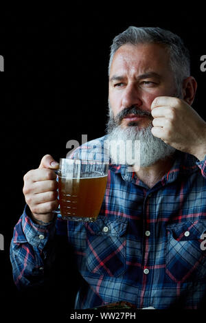 Brutale dai capelli grigi uomo adulto con la barba mangia la bistecca di senape e bevande birra, invita ad un pasto, il concetto di una vacanza, festival, Oktoberfest o San Pa Foto Stock