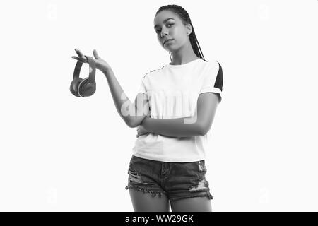 Ritratto di bella bruna africano ragazza adolescente con dreadlocks in sportswear ascoltando la musica attraverso le cuffie senza fili isolati su studio backgroun Foto Stock