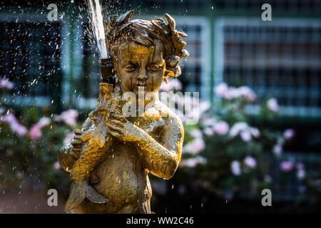 Giovane angelo d'oro con la pesca di alloro nella sua fontana. Foto Stock