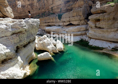 TOurist in piedi sulle scogliere al di sopra di un piccolo stagno di Wadi Fusc, Oman, Medio Oriente Foto Stock