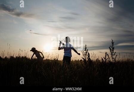 Silhouette di fratelli a giocare con piani di carta al di fuori al tramonto Foto Stock