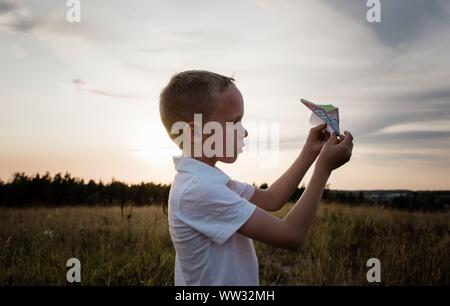 Profilo di un ragazzo giocando con un aeroplano di carta in un prato al tramonto Foto Stock