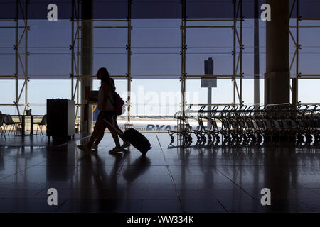 Passeggeri a piedi con i bagagli nel terminal dell'aeroporto, con Ryanair in aereo in background Foto Stock