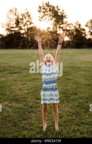 Felice di tween girl gettando fiori in aria al crepuscolo Foto Stock