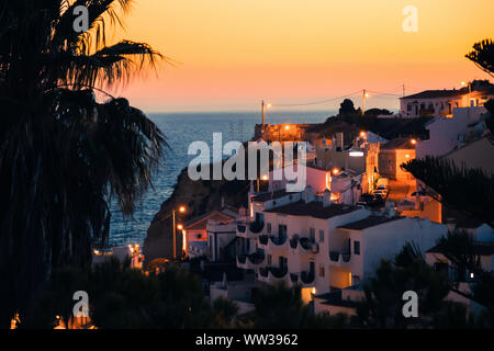 Bella vista di una palma, case mediterranee e un tramonto a Carvoeiro Beach in Algarve, PORTOGALLO Foto Stock