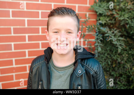 Felice preteen boy a sorridere di fronte a un muro di mattoni sulla giornata di sole Foto Stock