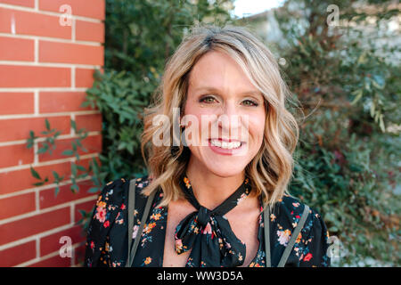 Ritratto di donna felice di fronte a un muro di mattoni giornata soleggiata in California Foto Stock