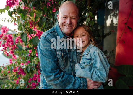 Felice papà abbracciando la figlia vicino a fiori di colore rosso Foto Stock