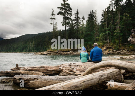 Momento di calma di uomo e bambino seduto su Log in prossimità di un lago Foto Stock