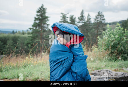 Ritratto di una donna avvolta in un sacco a pelo mentre camping all'aperto Foto Stock