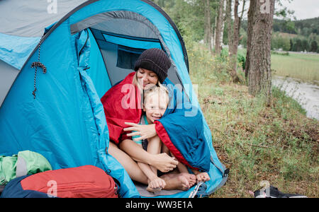 Madre e figlio seduti insieme sorridente in una tenda mentre camping in vacanza Foto Stock