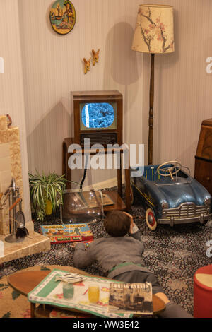 Una scena di un 1960 soggiorno o salotto con un ragazzo la posa sul pavimento a guardare un vintage in bianco e nero TV Foto Stock