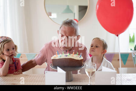 Il nonno si sedette con i suoi nipoti il giorno del suo compleanno candele di soffiatura Foto Stock