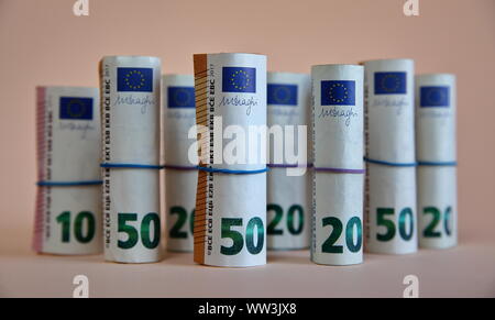 50, 20 e 10 le banconote in euro arrotolato in bobine e legato con blu e viola di gomma elastica isolati su color pastello sfondo vicino. Foto Stock