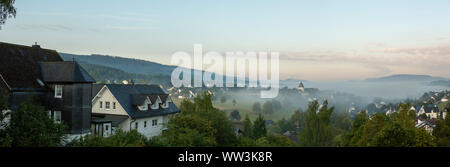 Ampia vista panoramica con basso appeso nebbia di mattina oltre la montagna villaggio termale di Grafschaft negli sport invernali regione di Sauerland, Germania Foto Stock