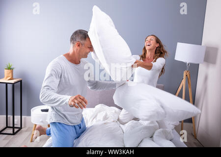 Coppia felice combattendo insieme con il Bianco di cuscini sul letto Foto Stock