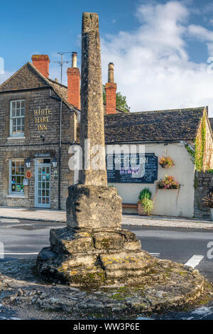 Con il suo 'Cross-Head' manca, questa struttura in pietra si erge al di fuori del White Hart Inn di Ashton Keynes. Un piccolo villaggio nel nord del Wiltshire, giace wi Foto Stock