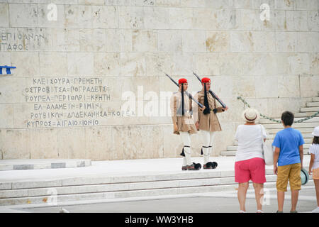 Atene GRECIA - Luglio 15 2019; turisti guardando la Guardia Presidenziale al di fuori del palazzo presidenziale e parete con carattere greco segni custodisce la tomba di Unk Foto Stock