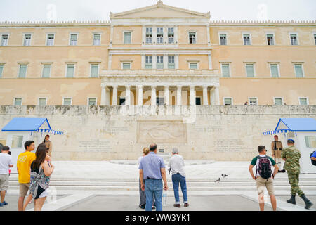 Atene GRECIA - Luglio 15 2019; i viaggiatori guardando la Guardia Presidenziale al di fuori del palazzo presidenziale e parete con caratteri greci guardie segni Tomba dell Onu Foto Stock