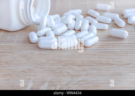 Bianco pillole mediche la fuoriuscita di un flacone di farmaco su un di legno sfondi. Foto Stock