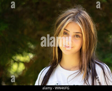 Bellezze naturali close up ritratto di una giovane donna su un sfocata foresta verde dello sfondo con mette in luce con i suoi capelli avente un atteggiamento. Foto Stock