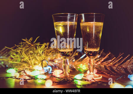 Bicchieri contro lo sfondo di una ghirlanda. Bere champagne in un ambiente romantico. La celebrazione del Natale e del nuovo anno insieme. Foto Stock