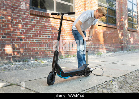 L'uomo il pompaggio di aria nel pneumatico sul suo E-scooter Foto Stock