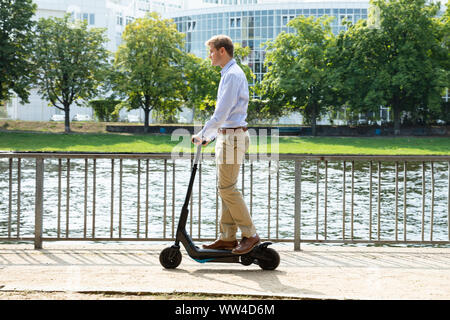 Giovane uomo che cavalca un elettrico Kick Scooter Foto Stock