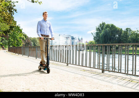 Giovane uomo che cavalca un elettrico Kick Scooter Foto Stock