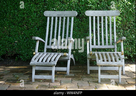 Due sedie a sdraio da giardino di teak di fronte ad una siepe verde nella luce del sole, Foto Stock