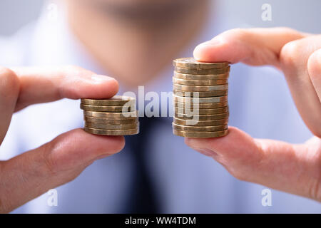 Uomo con due pile di monete da confrontare Foto Stock