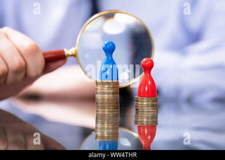 Uomo che guarda con lente di ingrandimento a due pile di monete. Divario di retribuzione tra donne e uomini Foto Stock