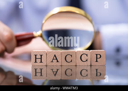 Uomo che guarda il sistema HACCP Lettere con lente di ingrandimento Foto Stock