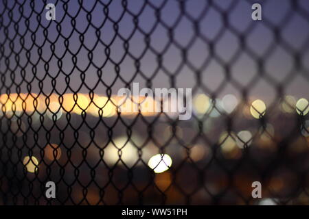Le luci della città attraverso un filo di maglia recinzione, Foto Stock