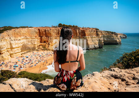 Giovane donna ammirando vista di scogliere, spiaggia e oceano turchese in spiaggia a Benagil, Algarve, Portogallo. Foto Stock