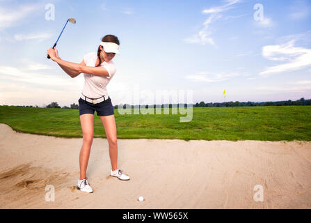 Donna giocatore di golf in sabbia trappola preparando per colpire la palla. Foto Stock