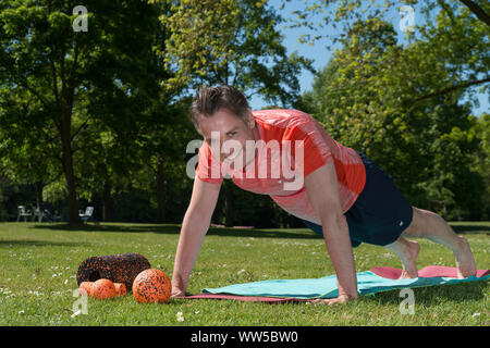 Uomo in abbigliamento sportivo nel parco, ginnastica, push-up sul tappetino Foto Stock