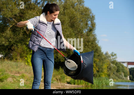 Donna di volontariato il prelievo di immondizia di plastica sulla costa del fiume. Pulizia il concetto di ambiente Foto Stock