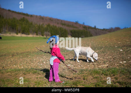 5-anno-vecchia ragazza con giacca rossa, blu velo e cane in un campo Foto Stock