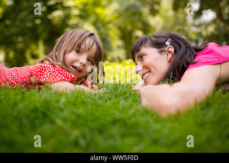 30-40 anni donna con il suo 4-6 anni figlia in rosso vestiti giacente in erba verde Foto Stock