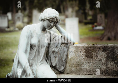 Una donna statua seduta su una pietra su un cimitero, Foto Stock