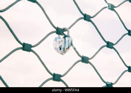 Un cuore con incisa la data appesi ad un filo di maglia recinzione, Foto Stock