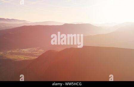 Il caldo sole di sunrise creeping oltre la linea di cresta del Derwent Fells e Newlands Beck nel Lake District inglese, UK. Foto Stock