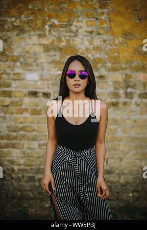 Ritratto di una giovane donna in piedi di fronte a un muro di mattoni Foto Stock