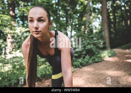 Femmina sportivo preparazione da eseguire nella foresta. Giovane atleta donna che guarda in avanti nella posizione di partenza per l'esecuzione. Ritratto di un fiducioso pareggiatore viene Foto Stock